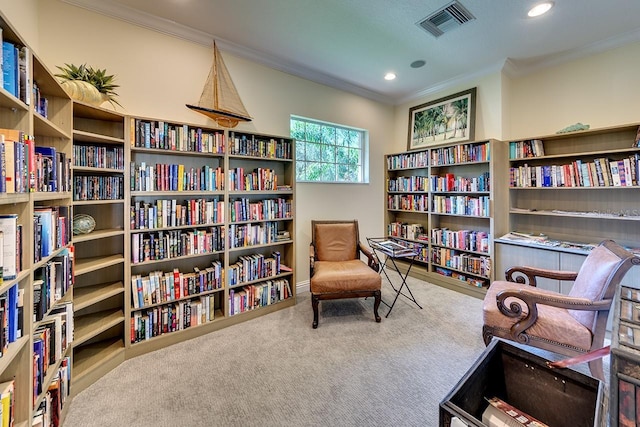 sitting room with bookshelves, carpet, visible vents, and crown molding