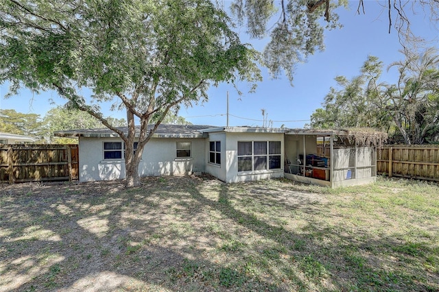 rear view of house with a sunroom, a fenced backyard, and stucco siding