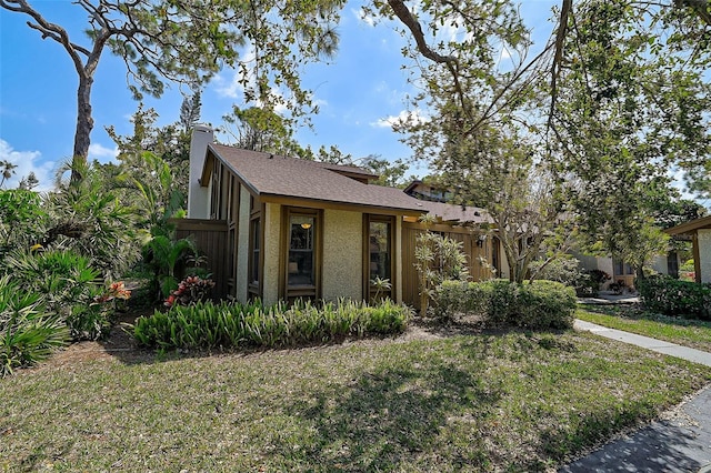 view of front of home featuring fence, a chimney, a front lawn, and stucco siding