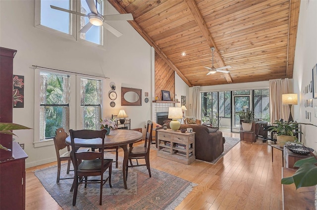 dining space with light wood-style floors, wooden ceiling, ceiling fan, a brick fireplace, and beam ceiling