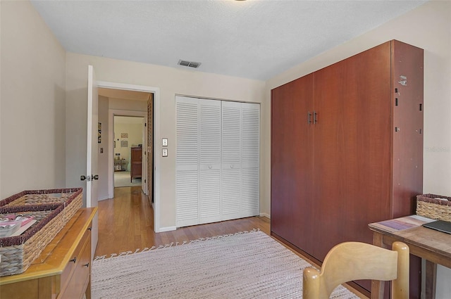 bedroom featuring a textured ceiling, a closet, wood finished floors, and visible vents