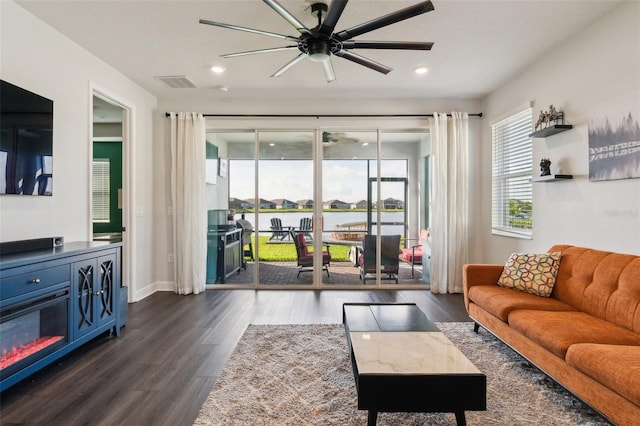 living room featuring plenty of natural light, dark wood-style flooring, visible vents, and a water view