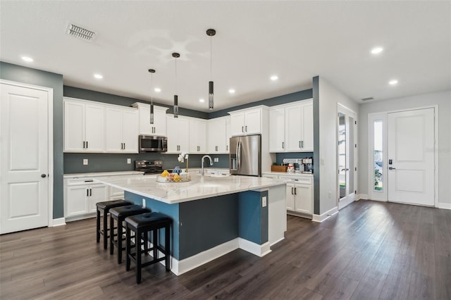 kitchen with a breakfast bar, dark wood-style flooring, stainless steel appliances, visible vents, and an island with sink