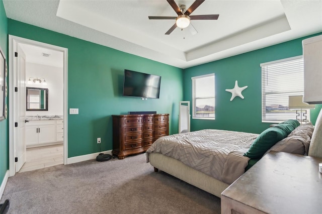 carpeted bedroom with a sink, a tray ceiling, ensuite bath, and baseboards