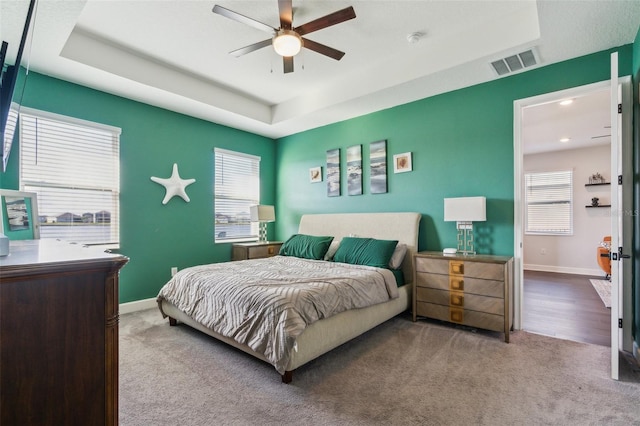 carpeted bedroom with a raised ceiling, visible vents, ceiling fan, and baseboards