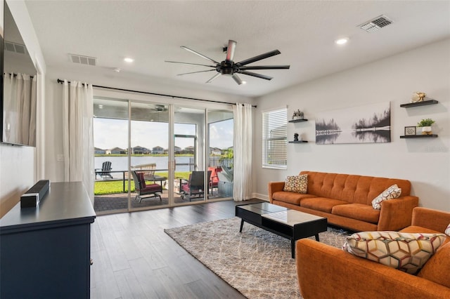 living room featuring ceiling fan, a water view, wood finished floors, and visible vents