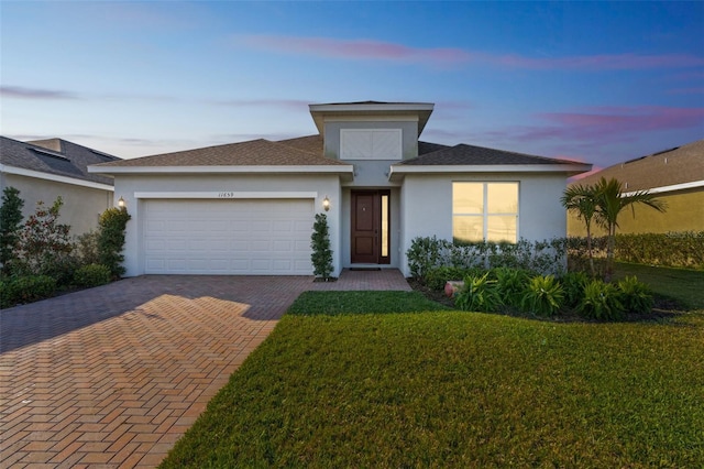 view of front of home with decorative driveway, a yard, an attached garage, and stucco siding