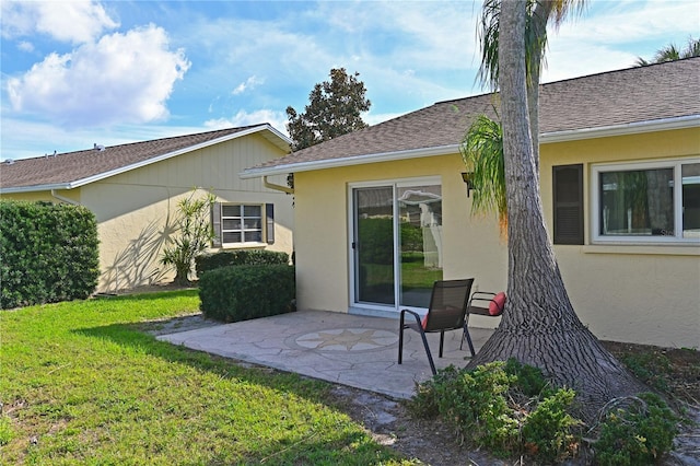 rear view of house with a patio area, a shingled roof, a yard, and stucco siding