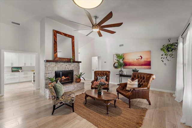 sitting room featuring light wood finished floors, visible vents, a brick fireplace, baseboards, and ceiling fan