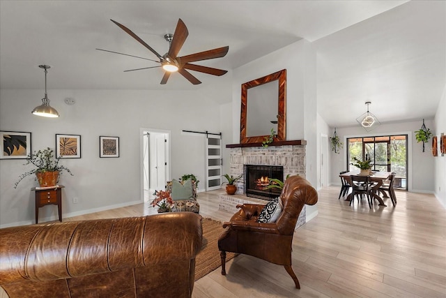 living area with high vaulted ceiling, light wood-style flooring, a ceiling fan, a barn door, and baseboards