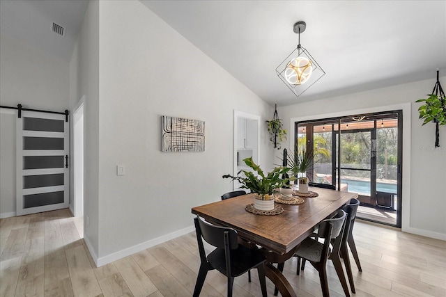 dining space with visible vents, baseboards, light wood-type flooring, a barn door, and high vaulted ceiling