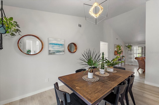 dining room featuring light wood-type flooring, baseboards, high vaulted ceiling, and visible vents