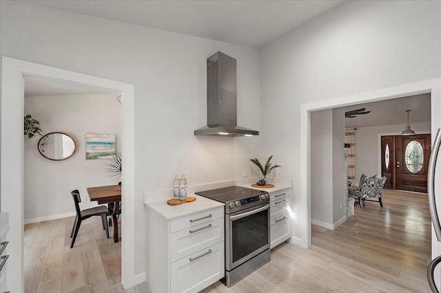 kitchen featuring stainless steel range with electric cooktop, light countertops, white cabinets, light wood-style floors, and wall chimney range hood