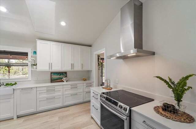 kitchen featuring ventilation hood, light wood-type flooring, light countertops, stainless steel range with electric cooktop, and white cabinets