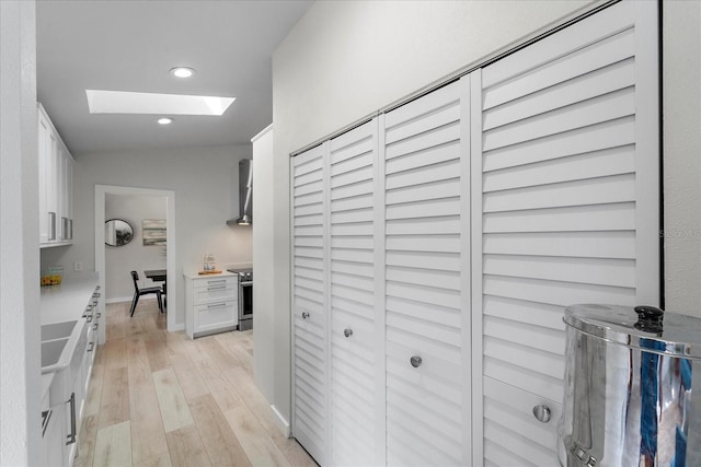 hall with a skylight, recessed lighting, light wood-style flooring, and baseboards