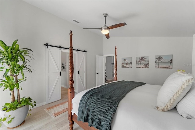 bedroom featuring visible vents, wood finished floors, a barn door, ceiling fan, and vaulted ceiling