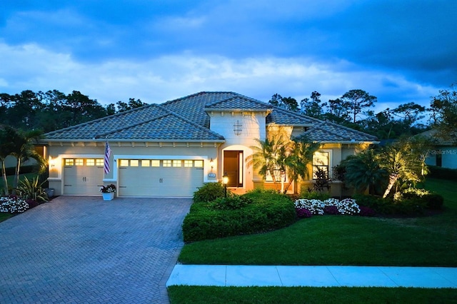 view of front facade featuring decorative driveway, stucco siding, an attached garage, a front yard, and a tiled roof