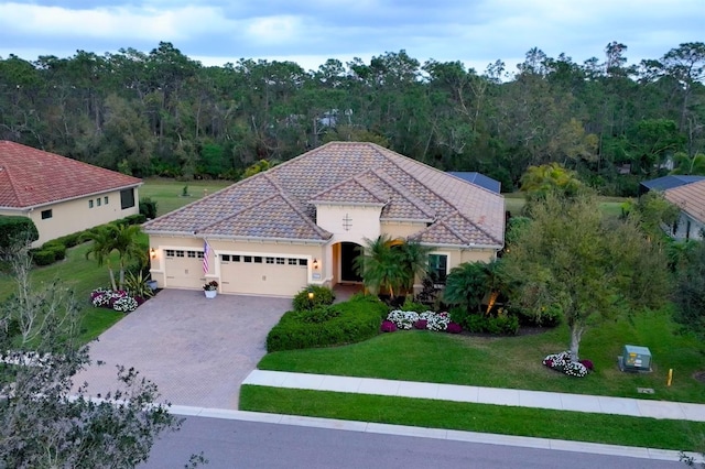 view of front of home with decorative driveway, a tile roof, an attached garage, a wooded view, and a front lawn