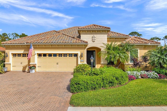 mediterranean / spanish house with decorative driveway, an attached garage, a front yard, and stucco siding