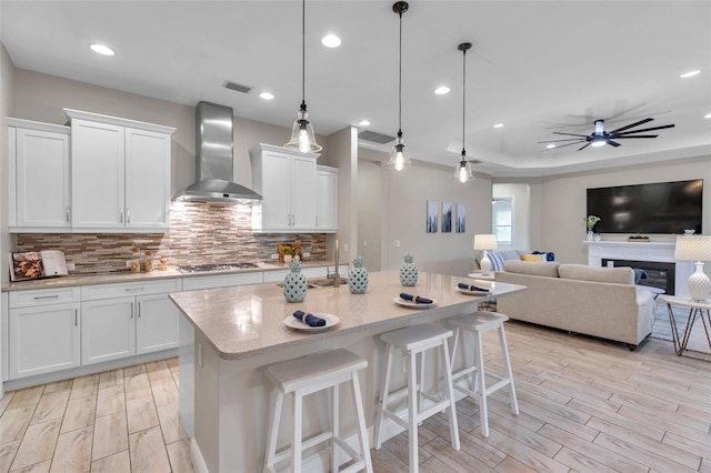 kitchen featuring wall chimney exhaust hood, stainless steel gas stovetop, decorative backsplash, and wood finish floors