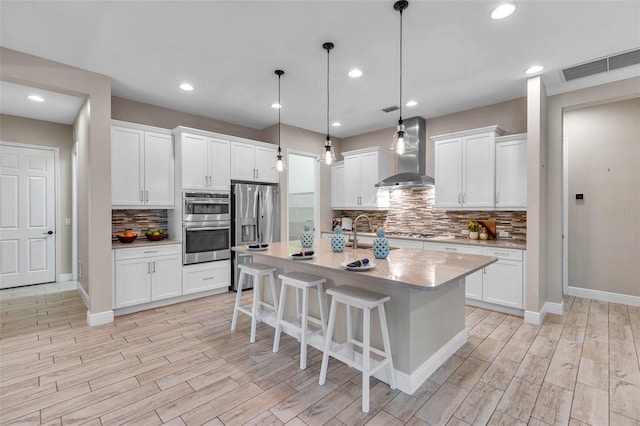 kitchen with visible vents, wall chimney exhaust hood, a kitchen breakfast bar, stainless steel appliances, and white cabinetry