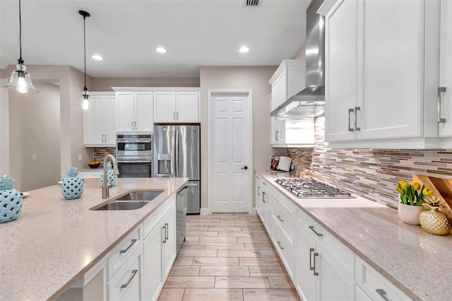 kitchen featuring stainless steel appliances, a sink, white cabinetry, wall chimney range hood, and pendant lighting