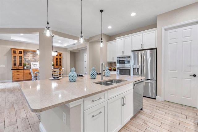 kitchen with an island with sink, a tray ceiling, stainless steel appliances, white cabinetry, and a sink