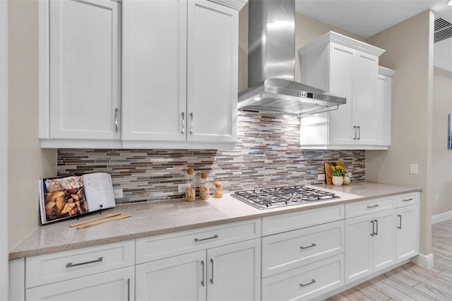 kitchen featuring stainless steel gas cooktop, light wood-style floors, white cabinets, wall chimney exhaust hood, and tasteful backsplash