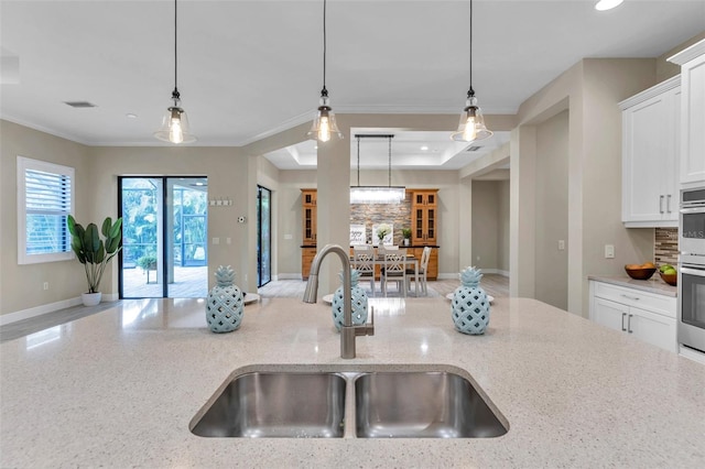 kitchen featuring visible vents, white cabinets, hanging light fixtures, light stone countertops, and a sink