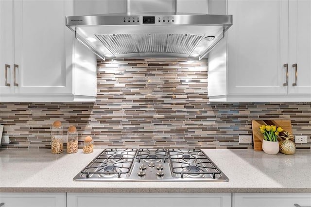 kitchen with wall chimney exhaust hood, stainless steel gas cooktop, white cabinets, and backsplash