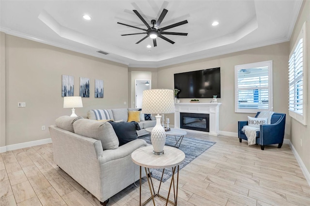 living room with visible vents, a raised ceiling, baseboards, ceiling fan, and light wood-style flooring