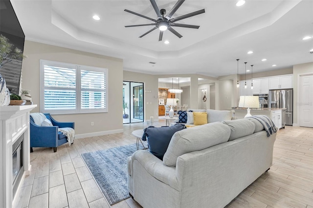 living area with a tray ceiling, a glass covered fireplace, ceiling fan, and wood tiled floor