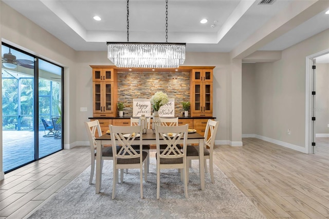 dining space featuring light wood-style floors, baseboards, and a raised ceiling