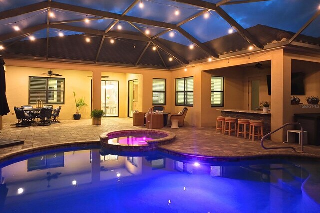 view of swimming pool with a ceiling fan, glass enclosure, outdoor dry bar, a patio area, and a pool with connected hot tub