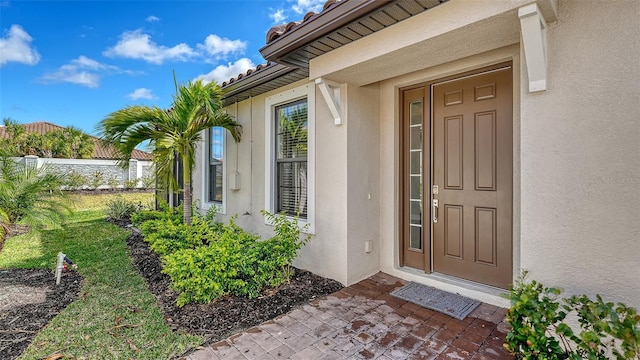 entrance to property with a tile roof, fence, and stucco siding