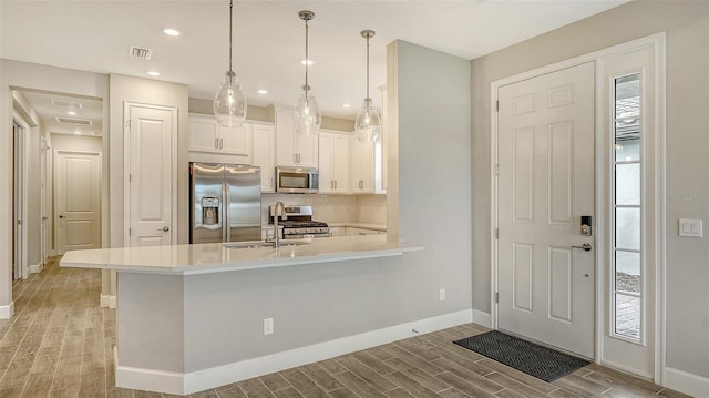 kitchen with stainless steel appliances, a sink, white cabinetry, backsplash, and wood tiled floor