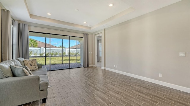 unfurnished living room featuring baseboards, a raised ceiling, and wood finish floors