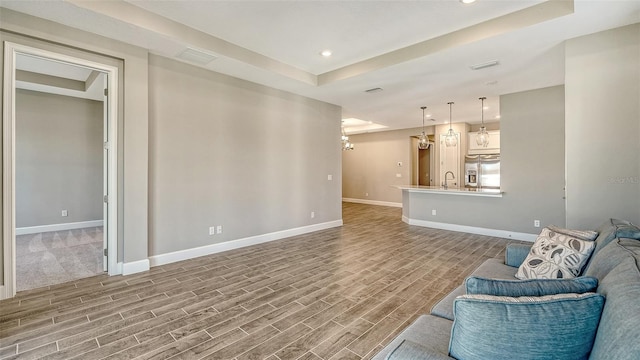 living area with a raised ceiling, wood finished floors, visible vents, and baseboards