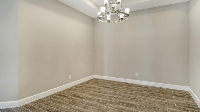 unfurnished room with baseboards, wood finish floors, and a notable chandelier