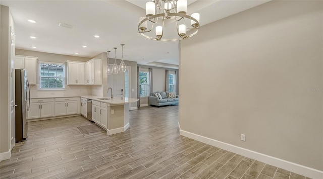 kitchen with light wood finished floors, open floor plan, a peninsula, stainless steel appliances, and a sink