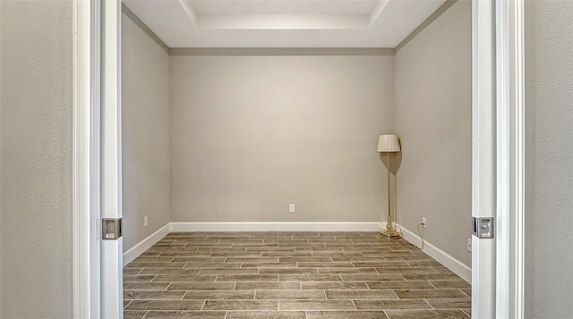 spare room with baseboards, a tray ceiling, and wood tiled floor