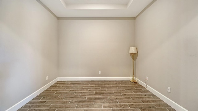 spare room featuring baseboards, a tray ceiling, and wood tiled floor