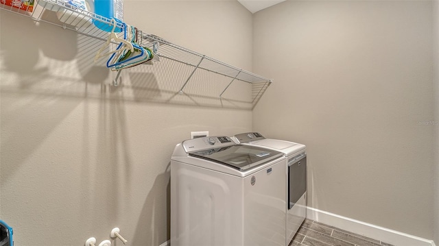 clothes washing area featuring laundry area, wood finished floors, washing machine and dryer, and baseboards