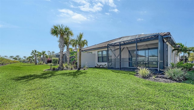 back of property featuring glass enclosure, a tile roof, and a lawn