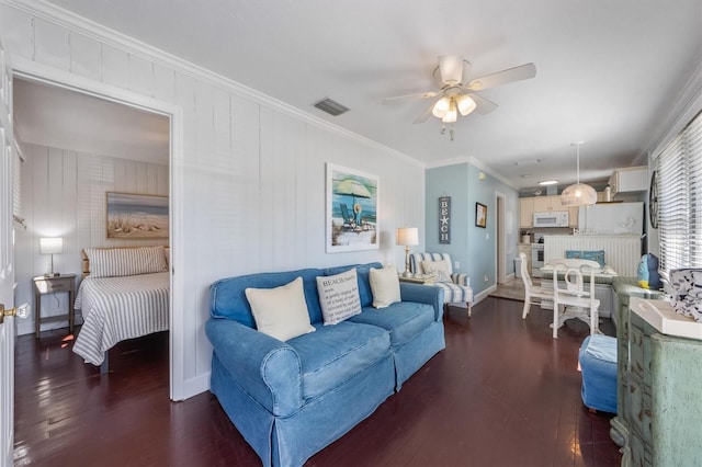 living room with ceiling fan, wood finished floors, visible vents, baseboards, and crown molding