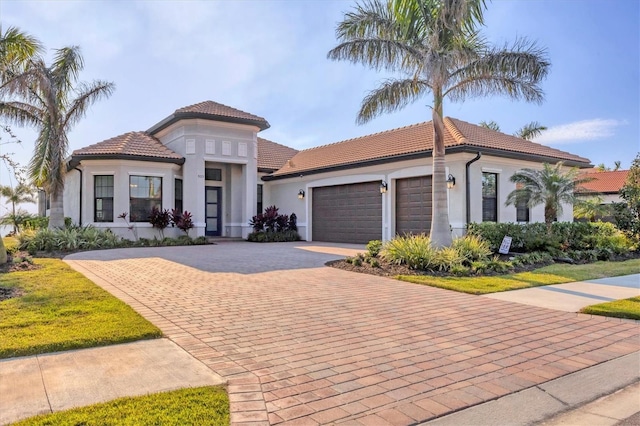 mediterranean / spanish-style house featuring a garage, decorative driveway, a tiled roof, and stucco siding