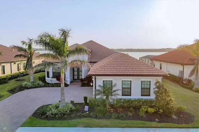 mediterranean / spanish-style home featuring decorative driveway, a tiled roof, a front lawn, and stucco siding