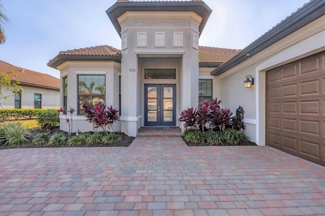 view of exterior entry with a garage, french doors, a tiled roof, and stucco siding