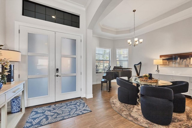 entrance foyer with ornamental molding, wood finished floors, a tray ceiling, french doors, and a notable chandelier