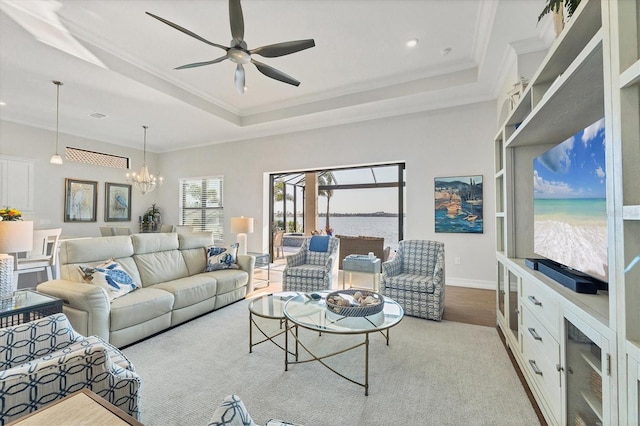 living area featuring a water view, ornamental molding, a raised ceiling, and ceiling fan with notable chandelier